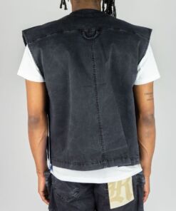 Back view of a person wearing a black sleeveless denim jacket over a white t-shirt.