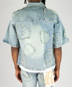 Back view of a person wearing a light blue denim shirt with frayed patches.